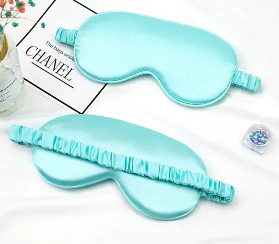 Light blue mulberry silk sleep mask with ruched elastic strap on white surface.